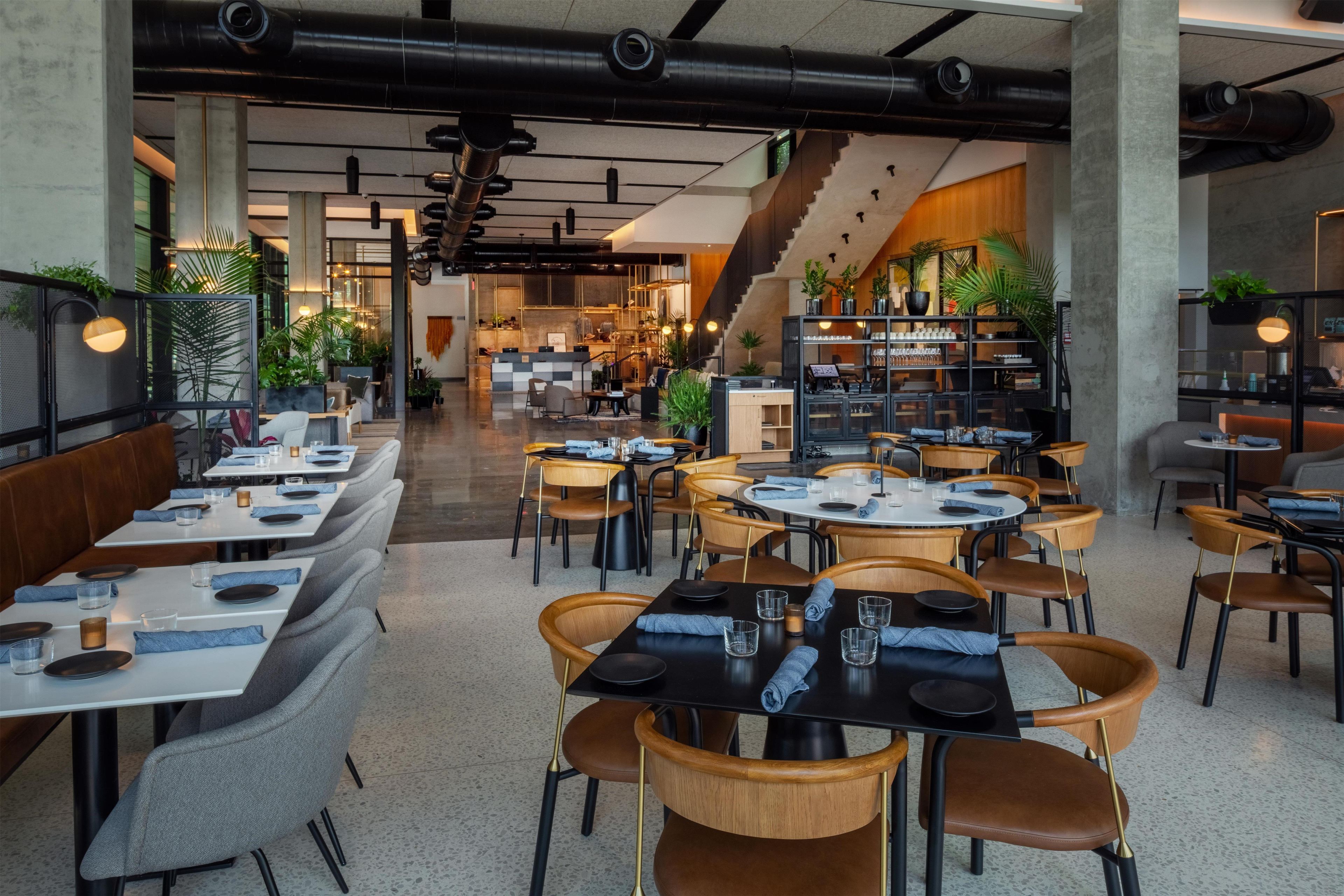 Een modern restaurantinterieur met verschillende zithoeken, waaronder ruimtes met zitbanken en tafels, en een zichtbare trap die naar een hoger niveau leidt.