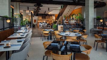 Een modern restaurantinterieur met verschillende zithoeken, waaronder ruimtes met zitbanken en tafels, en een zichtbare trap die naar een hoger niveau leidt.