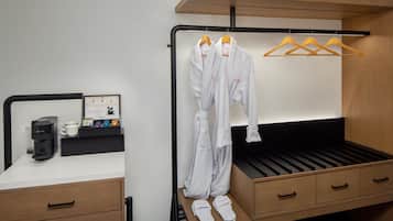 A modern hotel room with a bed, a coffee machine, a small table with a cup and a menu, and a wardrobe with hanging clothes.