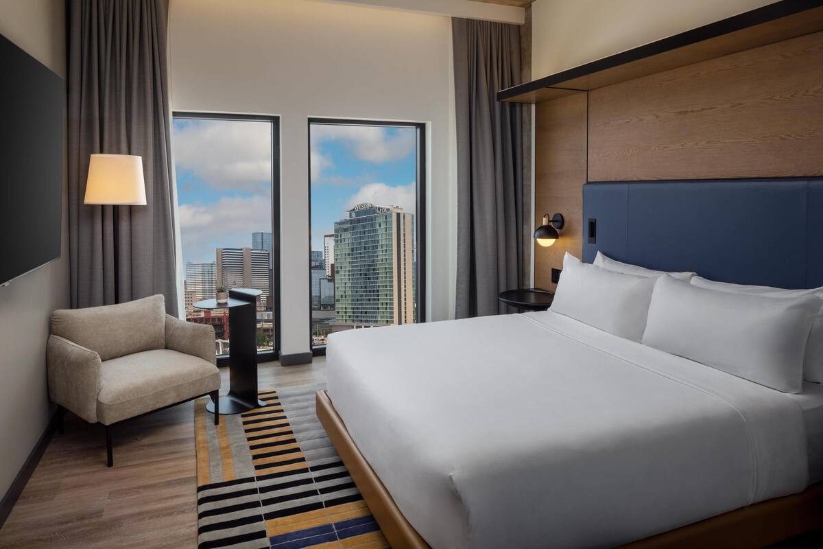 A hotel room with a large bed, a sofa, a TV, and a view of the cityscape.