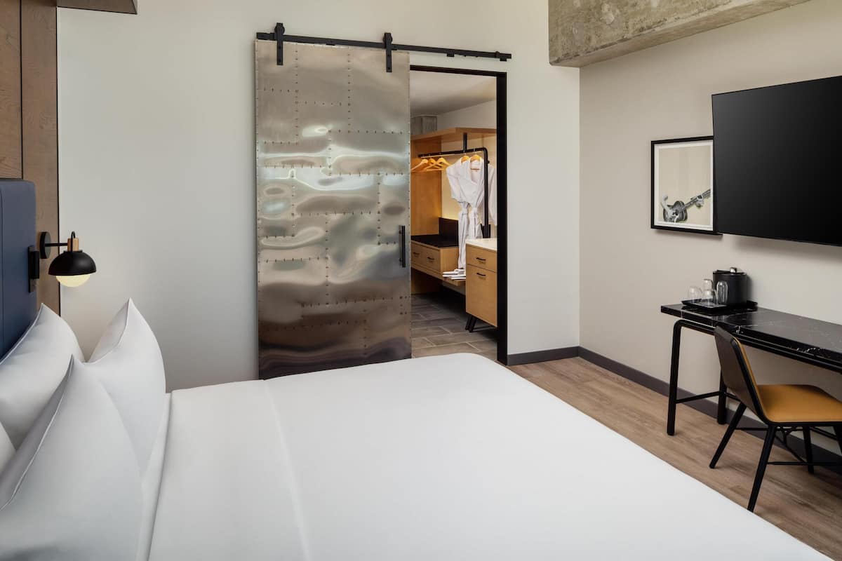 A hotel room with a bed, a desk with a chair, a wardrobe, and a television mounted on the wall.