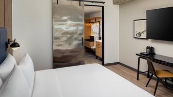A hotel room with a bed, a desk with a chair, a wardrobe, and a television mounted on the wall.