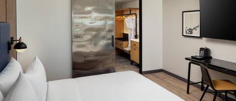 A hotel room with a bed, a desk with a chair, a wardrobe, and a television mounted on the wall.