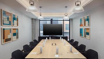 Una sala de conferencias con una larga mesa, sillas negras y una pantalla grande.