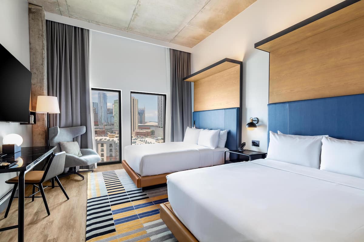 A hotel room with two beds, a desk, and a chair.