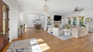 A spacious living room with a fireplace, a television, and a dining area with a wooden table and chairs. - 5BR 5BA Luxury Home with Private Pool on IOP! (Isle of Palms)