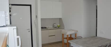A compact kitchen with white cabinets, a small countertop, and a dining table with chairs.