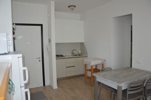 A compact kitchen with white cabinets, a small dining table, and a refrigerator. - Comfortable Flat Close to the Beach (Caorle)
