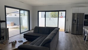 En moderne opholdsstue med en modulsofa, et træsofabord og et køkkenområde med et rustfrit stål køleskab.
