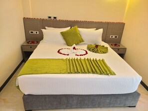 A neatly made bed with a green throw blanket, white pillows, and decorative flowers.