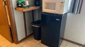 Een kleine kitchenette met een magnetron, een kleine koelkast, een prullenbak en een plank met een koffiezetapparaat en een doos.