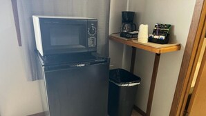 Eine kompakte Küchenzeile mit einem schwarzen Kühlschrank, einer Mikrowelle, einer Kaffeemaschine und einer kleinen Mülleimer.