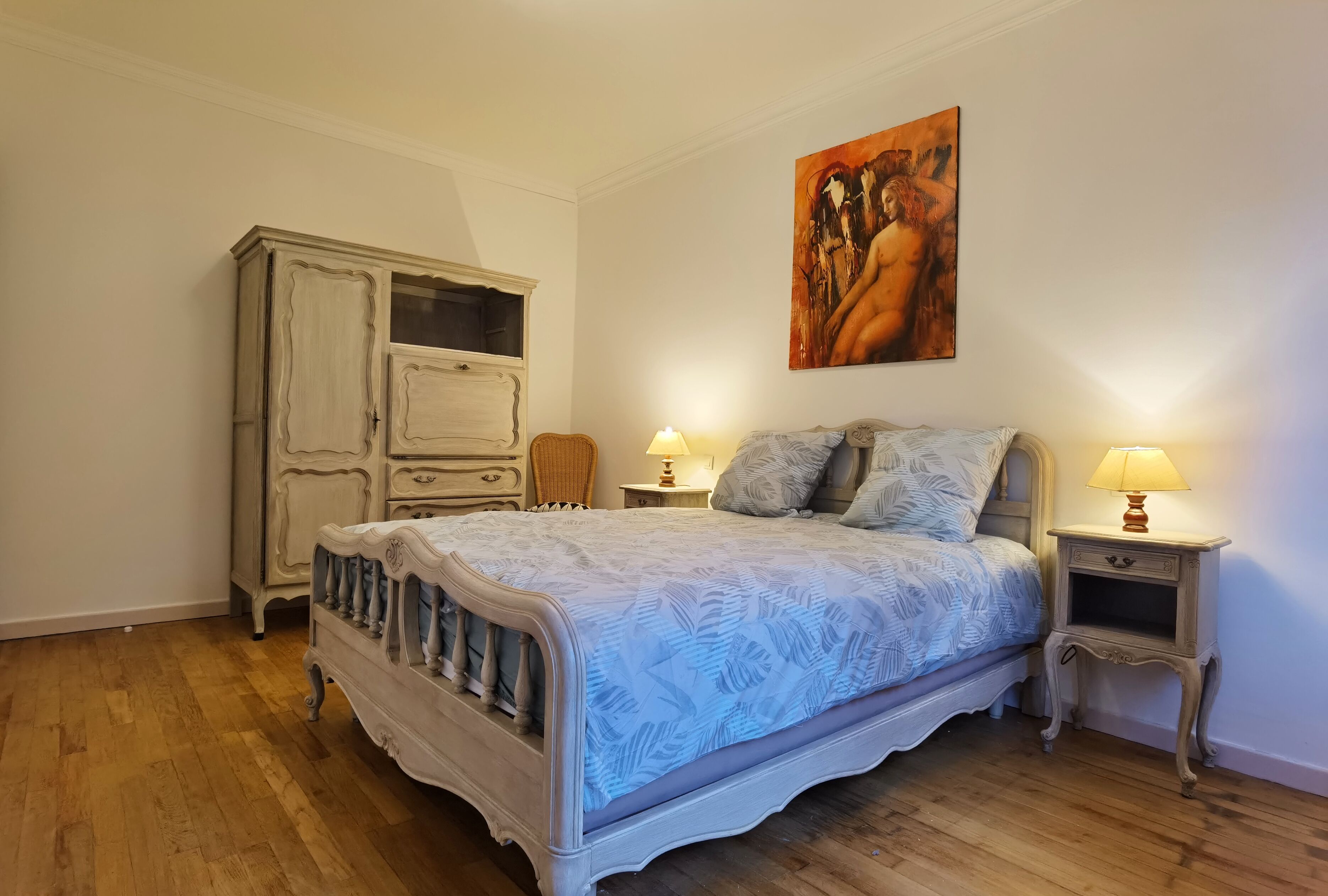 A bedroom with a bed, a dresser, a nightstand, and a painting on the wall.