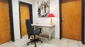Una habitación con escritorio, silla y lámpara. Hay tres puertas de madera y una obra de arte colgada en la pared.