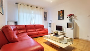 Una sala de estar moderna con un sofá de cuero rojo, una mesa de centro de vidrio, un mueble de televisión blanco y una planta en maceta.