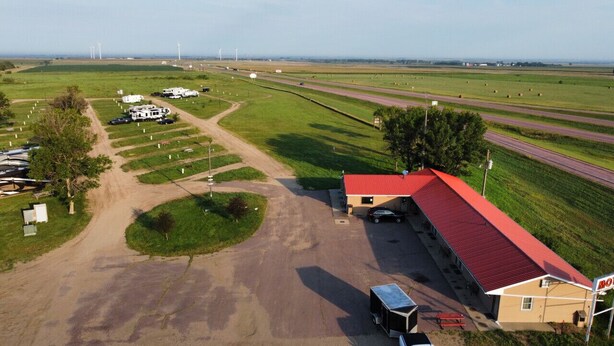 Vista aérea de una propiedad rural con un edificio de techo rojo, un camino de tierra y aerogeneradores a lo lejos.