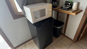 Una kitchenette compacta con un microondas sobre un refrigerador negro pequeño, una cafetera y un cesto de basura.