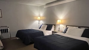 Ein Hotelzimmer mit zwei Betten, jedes mit einem Kissen und einer Lampe. Ein Stuhl mit einem Handtuch und einem Kleiderhaken sind ebenfalls vorhanden.