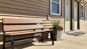 A wooden bench outside a building with beige siding and numbered doors. - White Lake Lodge - Family Room - Room 6 - Sleeps 5 (White Lake)