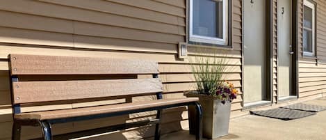 A wooden bench outside a building with beige siding and numbered doors.