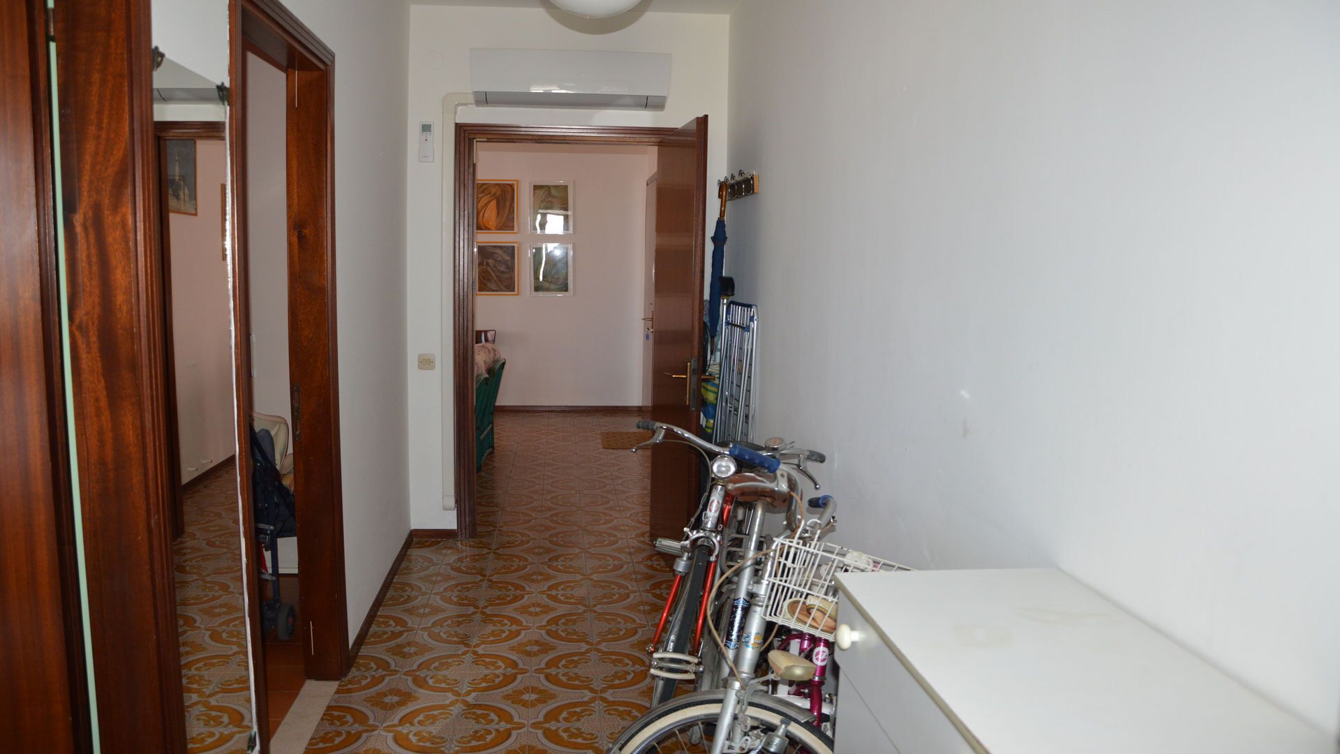 Un couloir avec un sol à motifs, un vélo et une porte donnant sur une autre pièce.