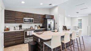 A modern kitchen with dark wood cabinets, stainless steel appliances, and a central island with bar stools.