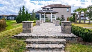 A paved pathway leading to a gazebo with stone steps, surrounded by greenery and residential buildings.