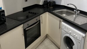 A compact kitchen with a stove, oven, sink, and washing machine. - Lovely 1-bed Apartment in Salford (Salford)