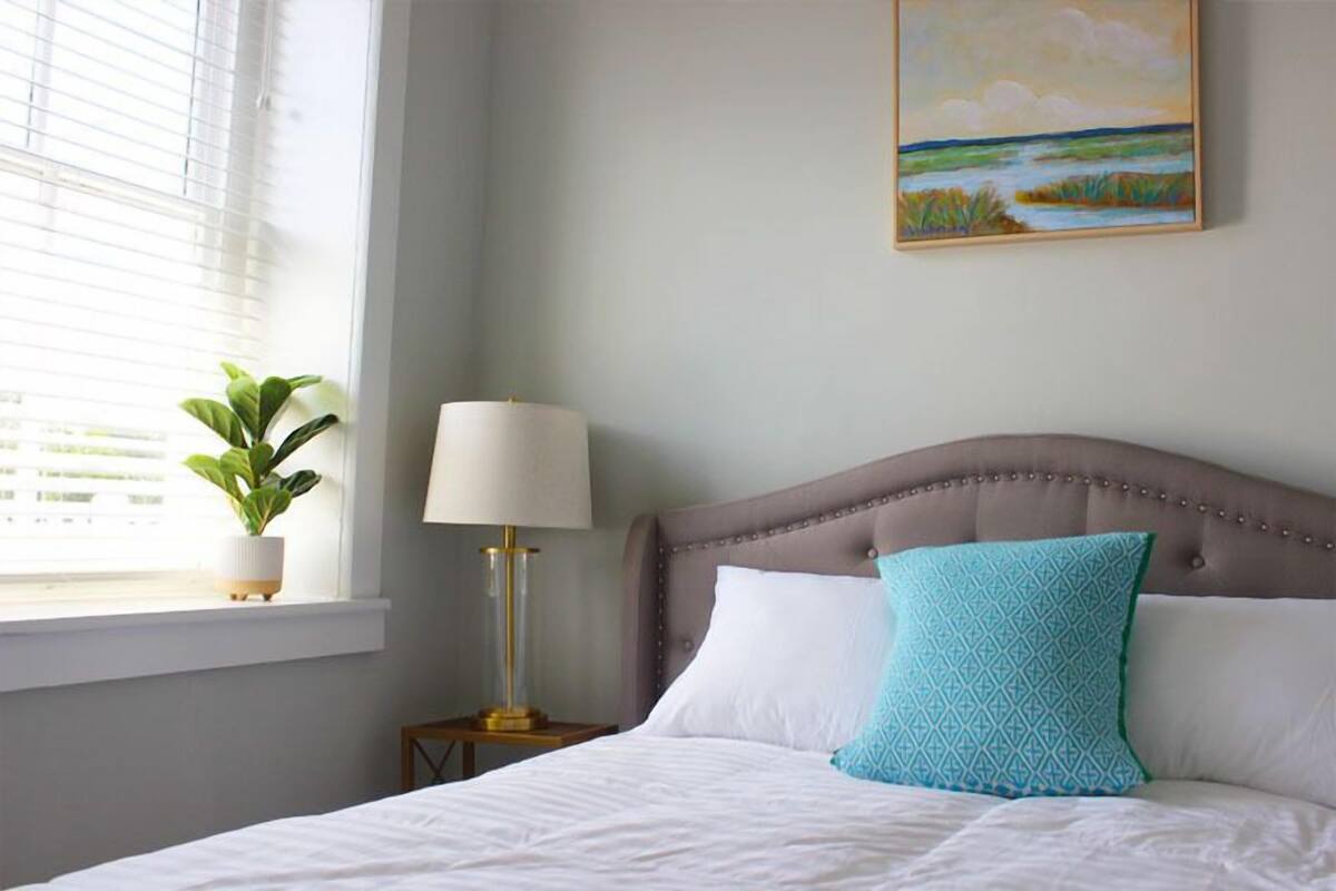 A neatly made bed with white linens, a blue patterned pillow, and a beige headboard.