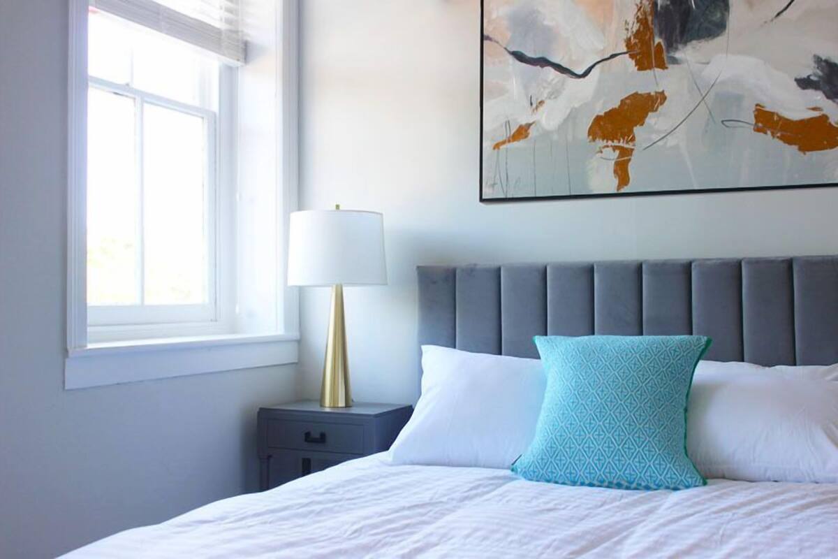 A bedroom with a bed, a nightstand, a lamp, and a large abstract painting on the wall.