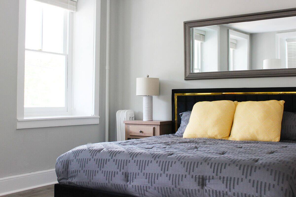 A bedroom with a bed, a nightstand, a lamp, and a mirror.