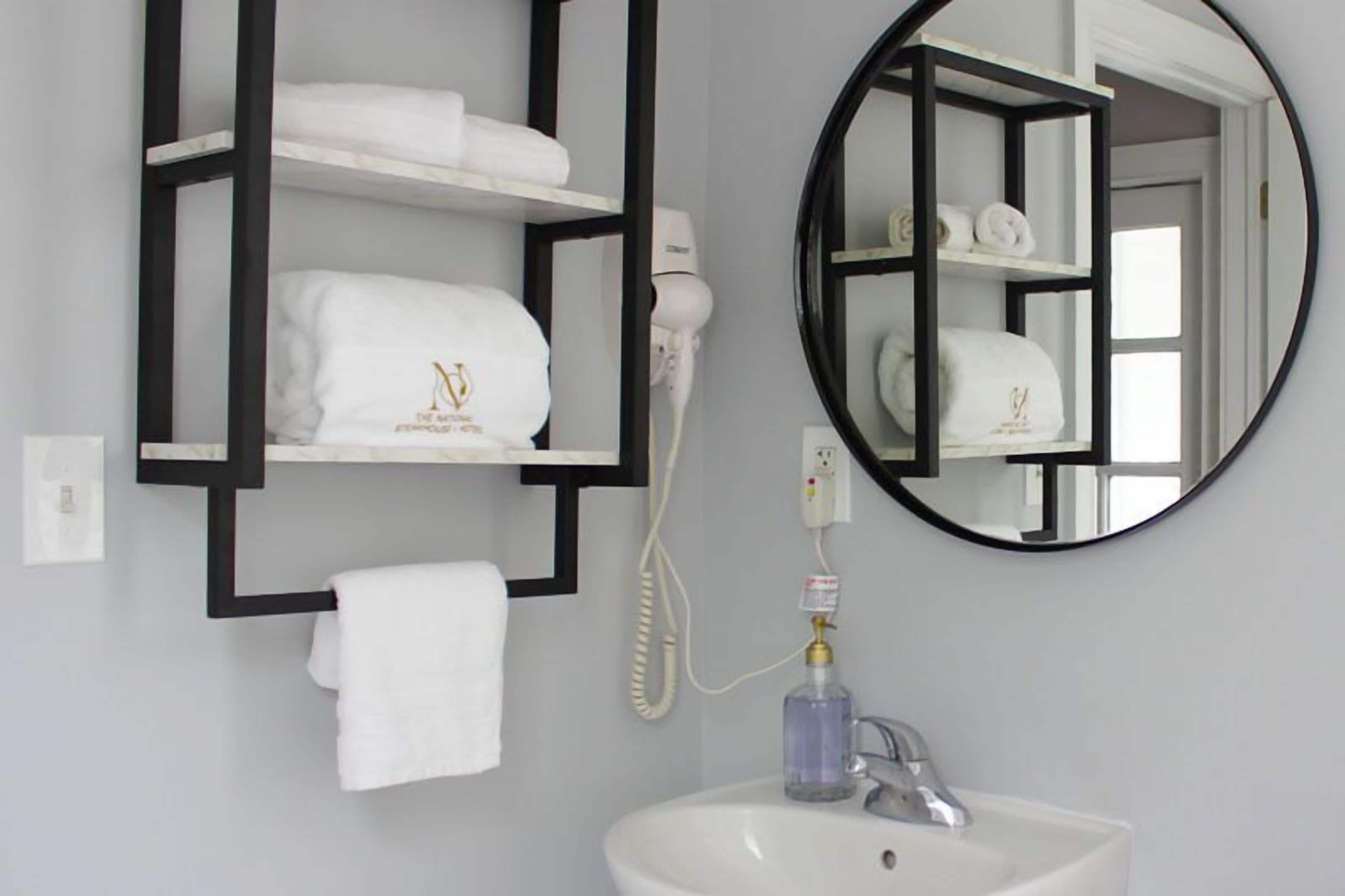 A bathroom with a white sink, a round mirror, and black shelves holding white towels.