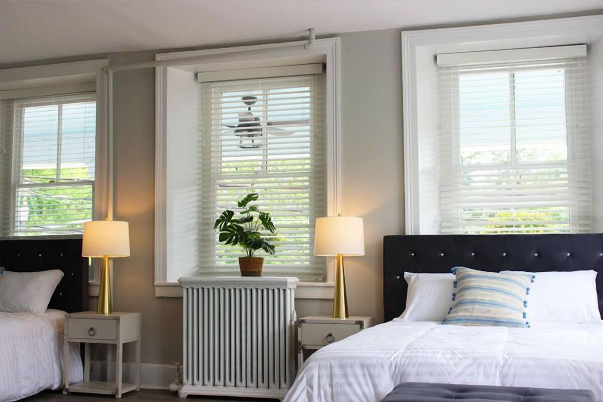 A hotel room with two beds, a radiator, a potted plant, and two bedside lamps.