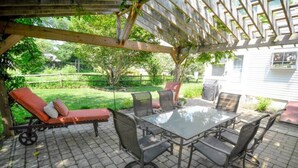 An outdoor patio with a glass-top table and chairs, a red cushioned lounge chair, and a pergola overhead. - The Big Belle of Bethlehem (Bethlehem)