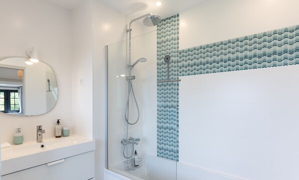 Un baño moderno con ducha envuelta en vidrio, tocador blanco con espejo y pared con diseño.