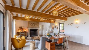 Un salon chaleureux avec des poutres apparentes, une cheminée et un coin repas comprenant une table et des chaises.