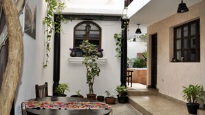 A courtyard with a round table, chairs, potted plants, and a hanging light fixture.