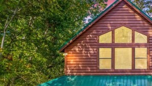 A wooden cabin with a green roof, a covered porch, and a garage.