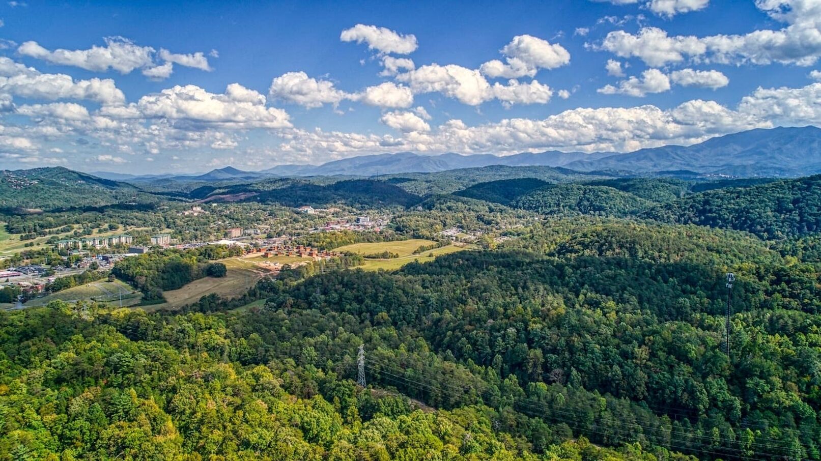 Vista panorámica de un pueblo ubicado en un valle, con colinas boscosas y densas al fondo.