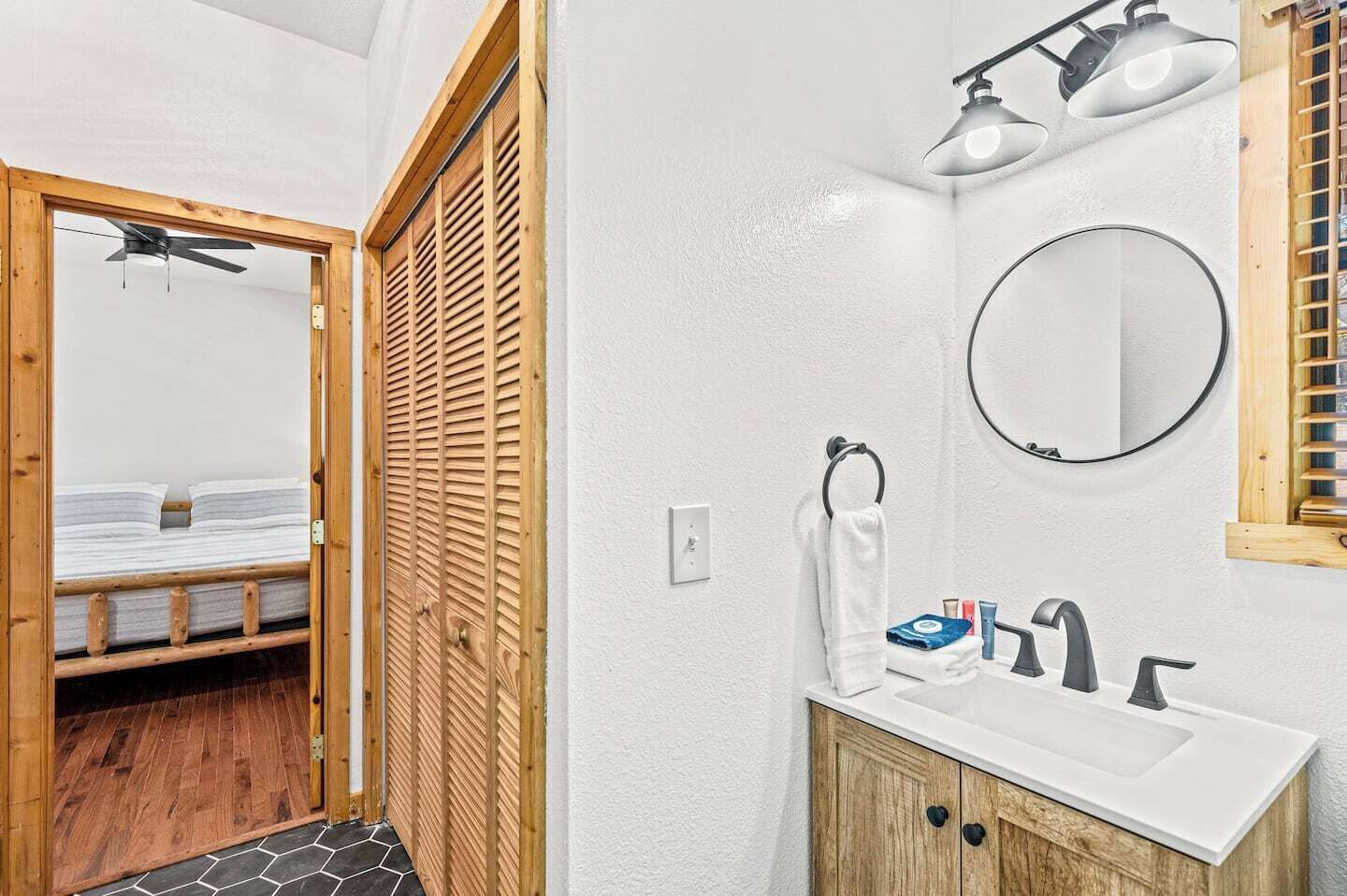Ein Badezimmer mit Holztür, einem Bett, einem weißen Waschbecken, einem Spiegel und einem Deckenventilator.