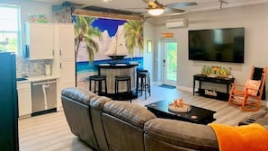A living room with a sofa, a coffee table, a TV, and a mural of palm trees. - Private Guest Suite with Shared Pool Access - just 9 miles from Boca Grande (Port Charlotte)
