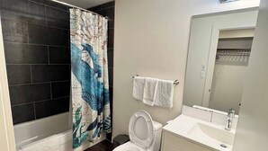 A bathroom with a bathtub, toilet, sink, and a shower curtain with a blue and white design. - Dt 1bed 1bath Cozy Suite 8 Min Walk To Arena (Edmonton)