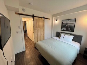 Un dormitorio con cama, una puerta de madera, un cuadro enmarcado y un pasillo que conduce a otra habitación.