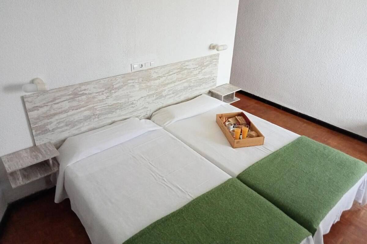 A double bed with white linens and a green throw blanket, a wooden bedside table, and a tray with toiletries.