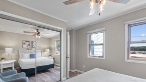 Un dormitorio con cama, ventilador de techo, ventana y vistas al exterior.