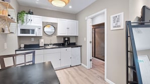 A modern kitchen with white cabinets, a round mirror, a built-in microwave, and a coffee maker.