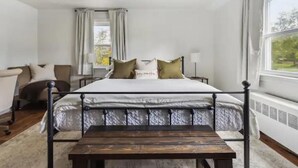 Quarto com cama, mesa de cabeceira, abajur e vista para o exterior.
