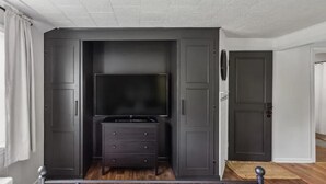 Quarto com guarda-roupa escuro, televisão de tela plana e cômoda pequena.