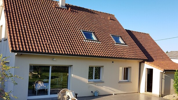 Een tweelaags huis met een pannendak, een overdekte patio met tuinmeubilair en een gazon.