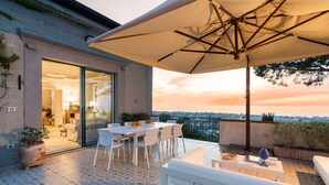 Une terrasse dotée d’un espace repas, de sièges extérieurs et offrant une vue sur la ville au coucher du soleil.
